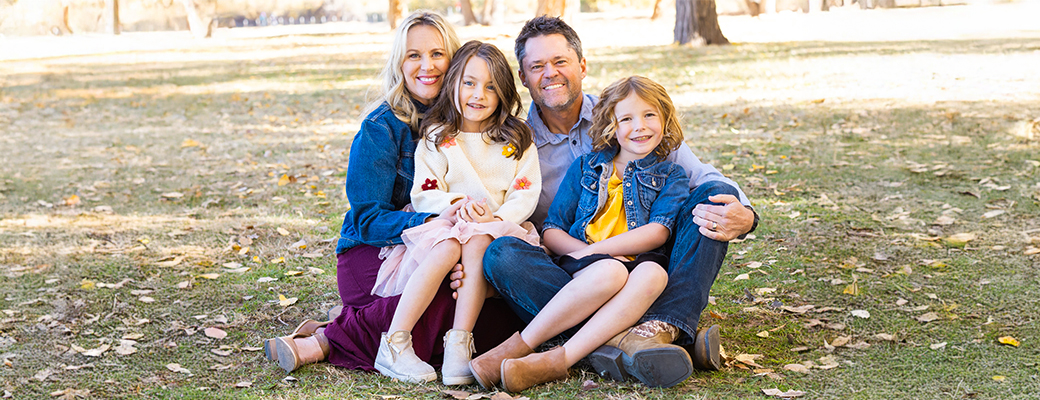 Image of Justin Osmond sitting in the grass with his wife and two daughters